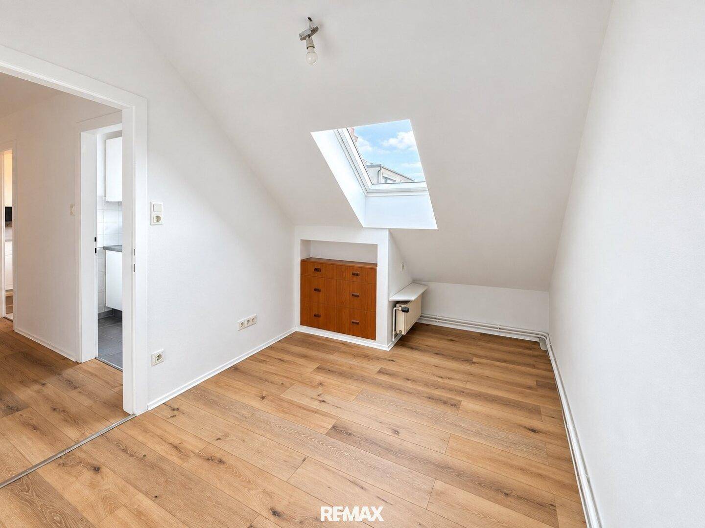 Helles Zimmer mit Holzboden, Dachschräge und Dachfenster, mit Zugang zur Küche.