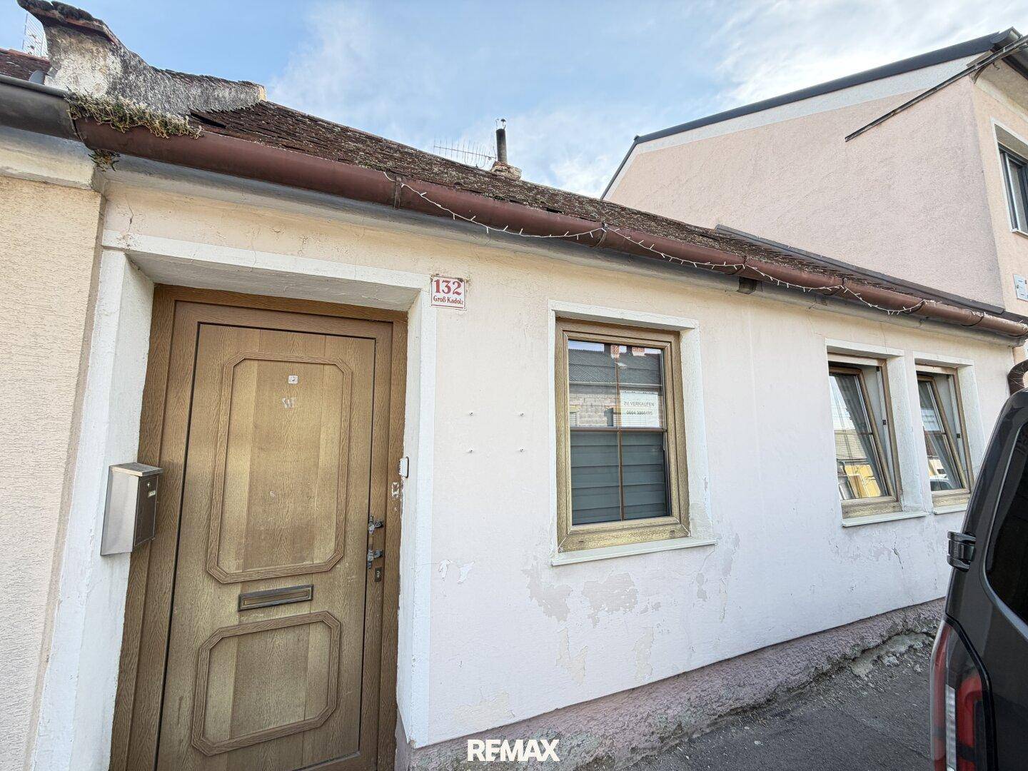 Vorderansicht eines älteren Hauses mit Holztür und kleinen Fenstern, direkt an der Straße gelegen.