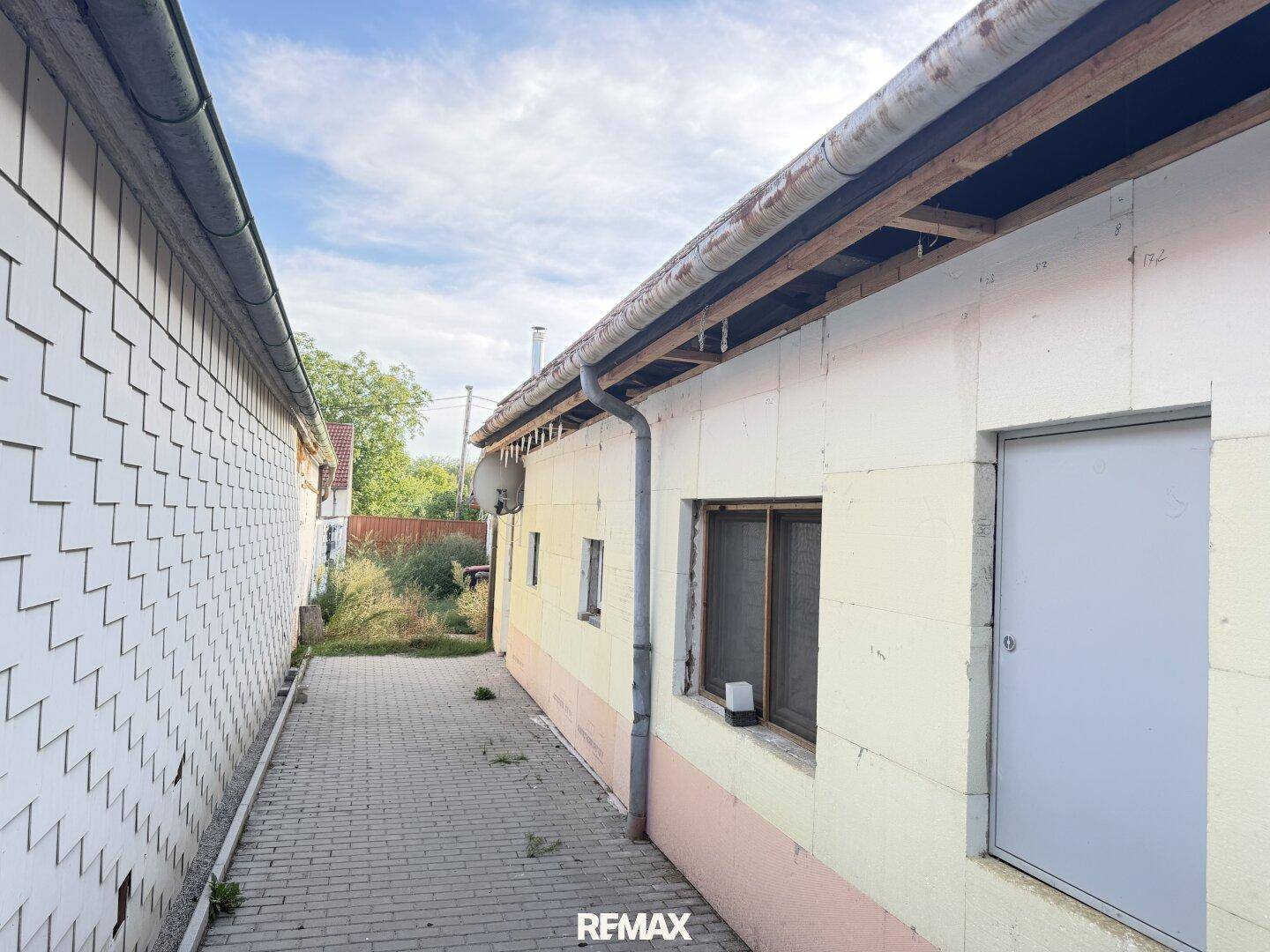 Seitenansicht eines Gebäudes mit schmalem gepflastertem Weg und einfacher Fassade.