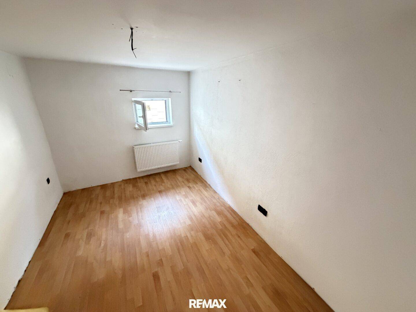 Helles Schlafzimmer mit Holzboden und einem Fenster, das viel Tageslicht hereinlässt.