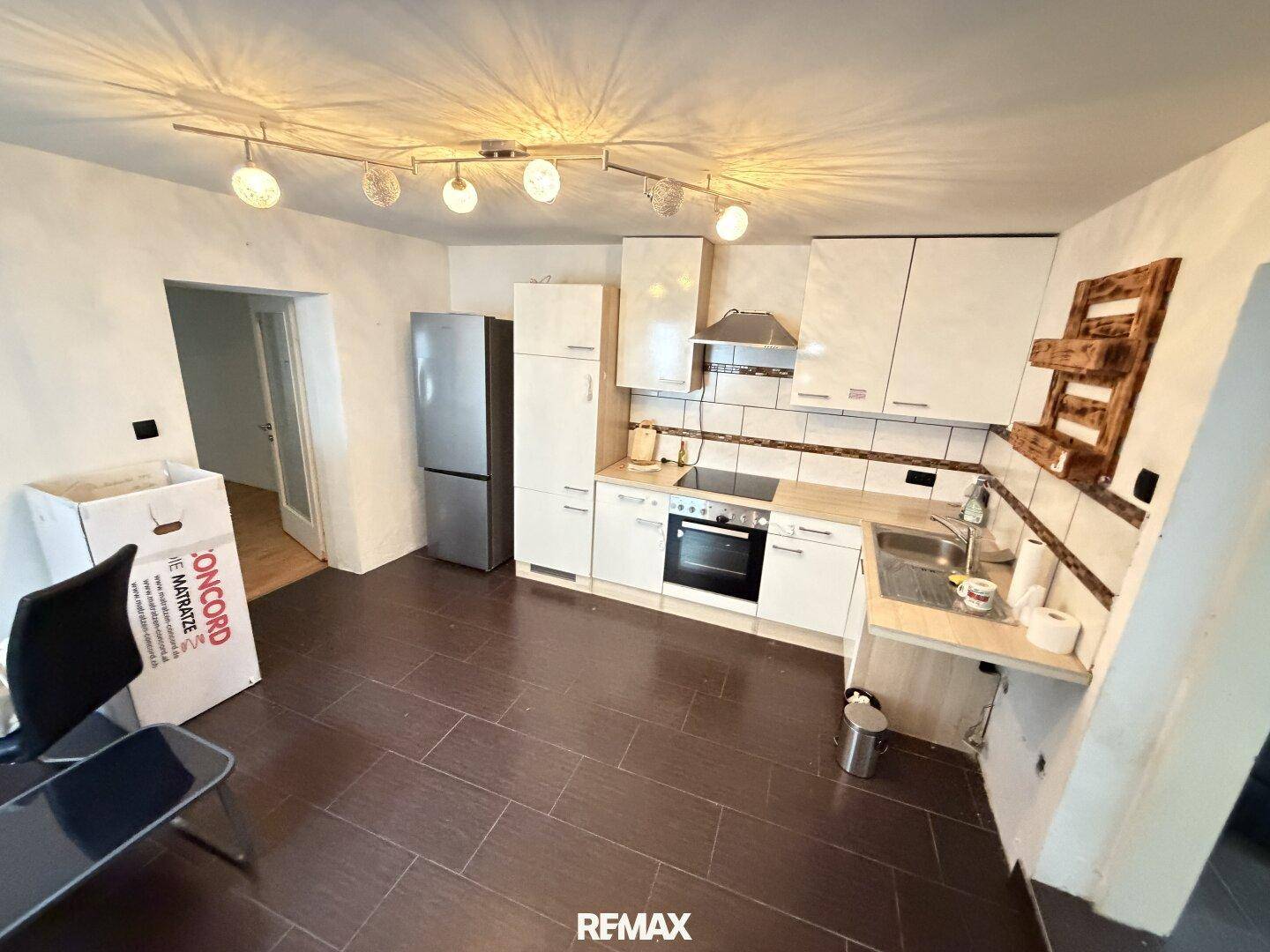 Küche mit dunklen Fliesen, weißen Schränken und einem freistehenden Kühlschrank, bereit zur Modernisierung.