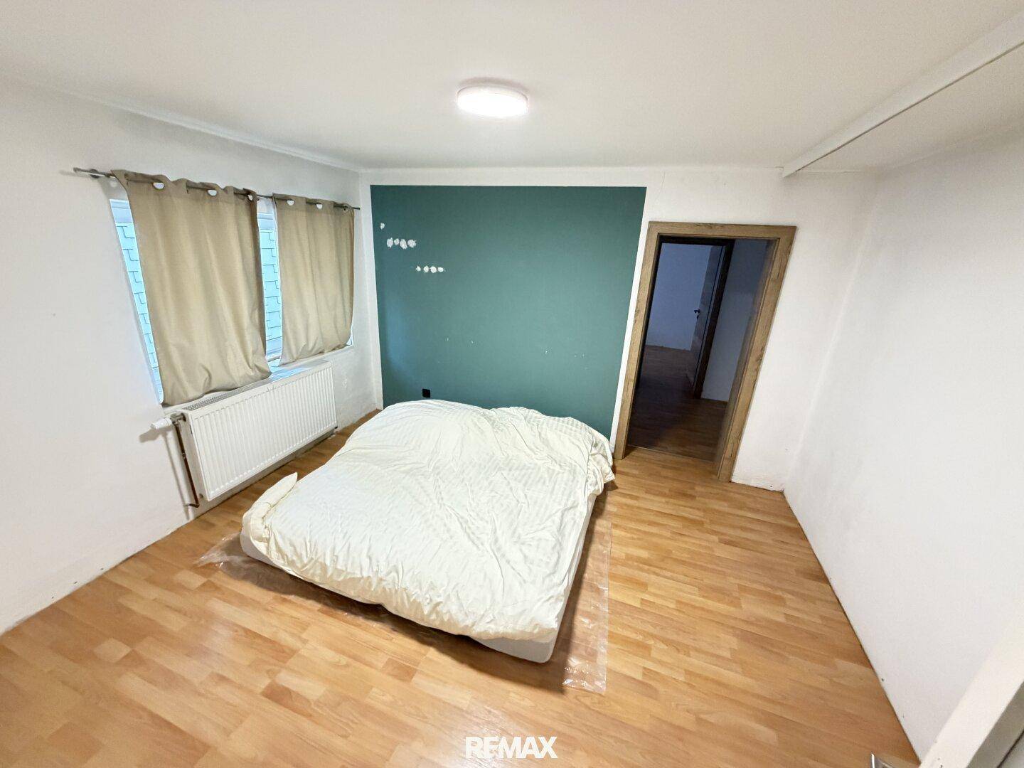 Schlafzimmer mit Holzboden, einer grünen Akzentwand und einem großen Fenster für natürliches Licht.