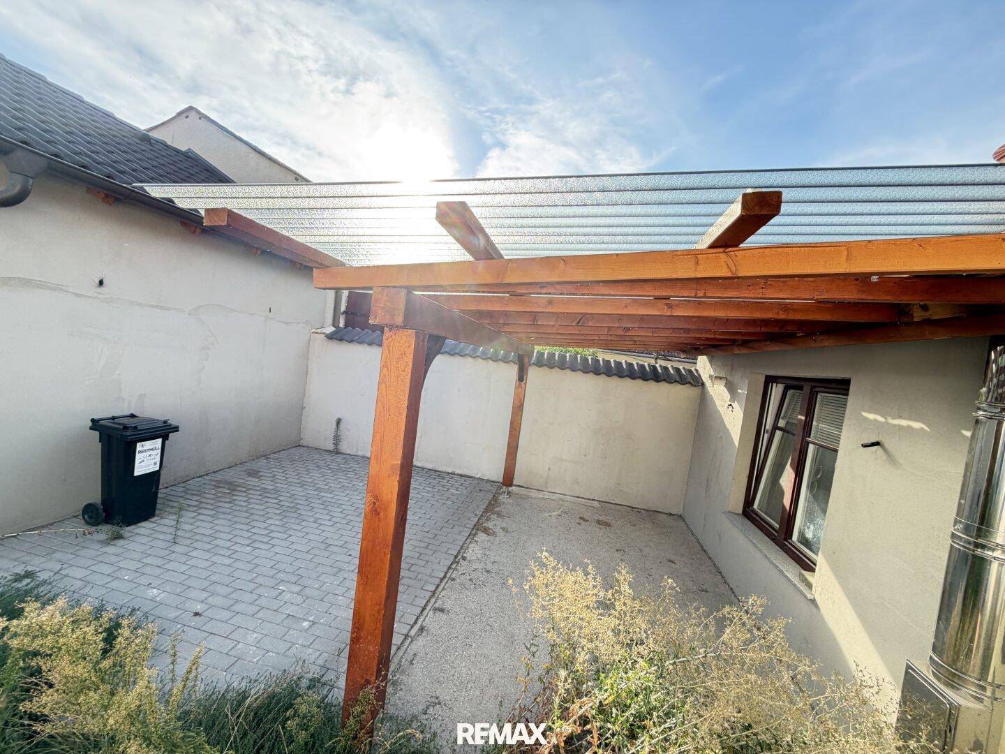 Gepflasterte Terrasse mit Holzpergola, die Schutz vor der Sonne bietet, unter blauem Himmel.