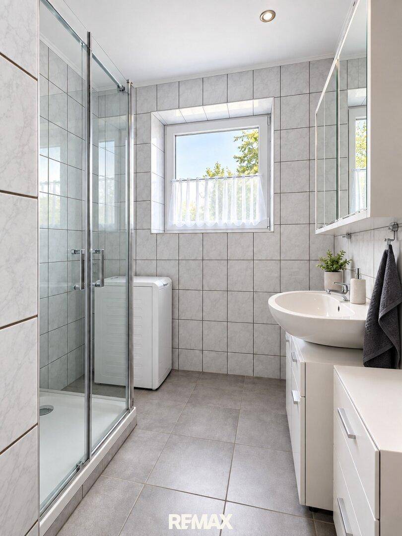 Modernes Badezimmer mit Duschkabine, Waschbecken, Waschmaschine und hellen Fliesen.