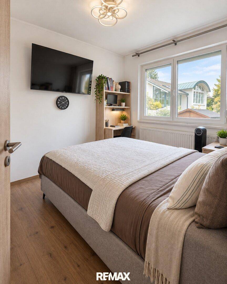 Helles Schlafzimmer mit Holzboden, Schreibtisch und an der Wand montiertem Fernseher.