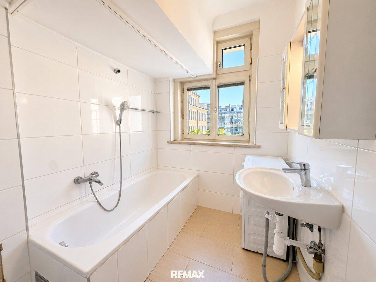Badezimmer mit Badewanne, Waschbecken, Waschmaschine und Fenster für natürliche Belüftung.