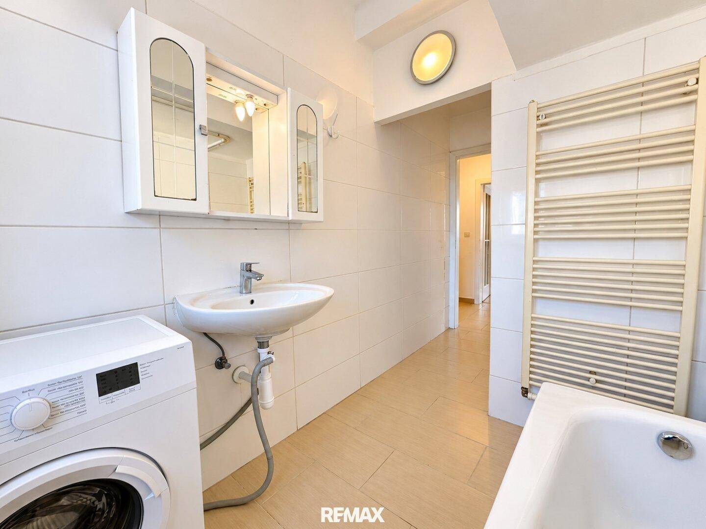 Badezimmer mit Waschbecken, Waschmaschine, beheiztem Handtuchhalter und Spiegelschrank.