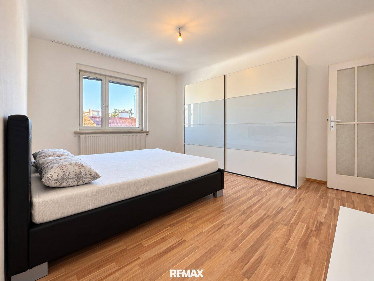 Schlafzimmer mit modernem schwarzen Bett, großem Schiebeschrank und Holzboden.