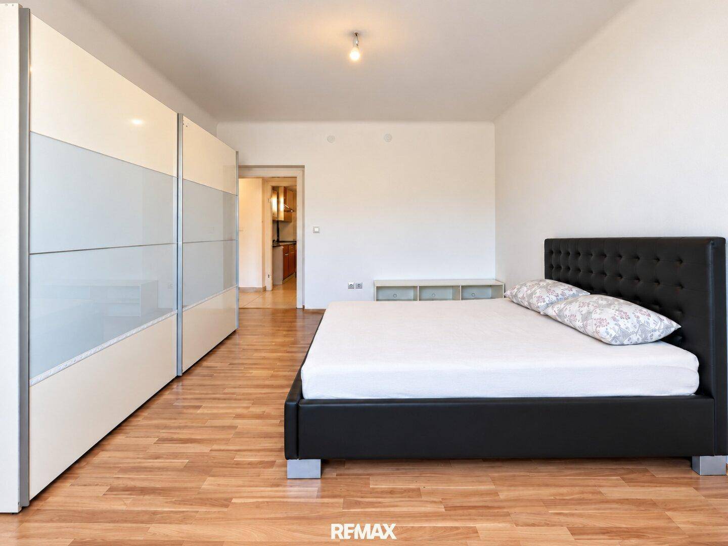 Schlafzimmer mit großem Schiebeschrank und schwarzem Bett, mit Zugang zu einem weiteren Raum.