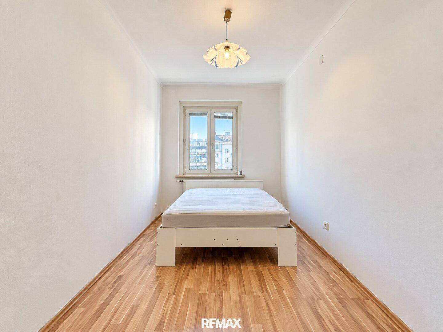 Kleines, helles Schlafzimmer mit weißem Bett und Fenster, das viel Tageslicht spendet.