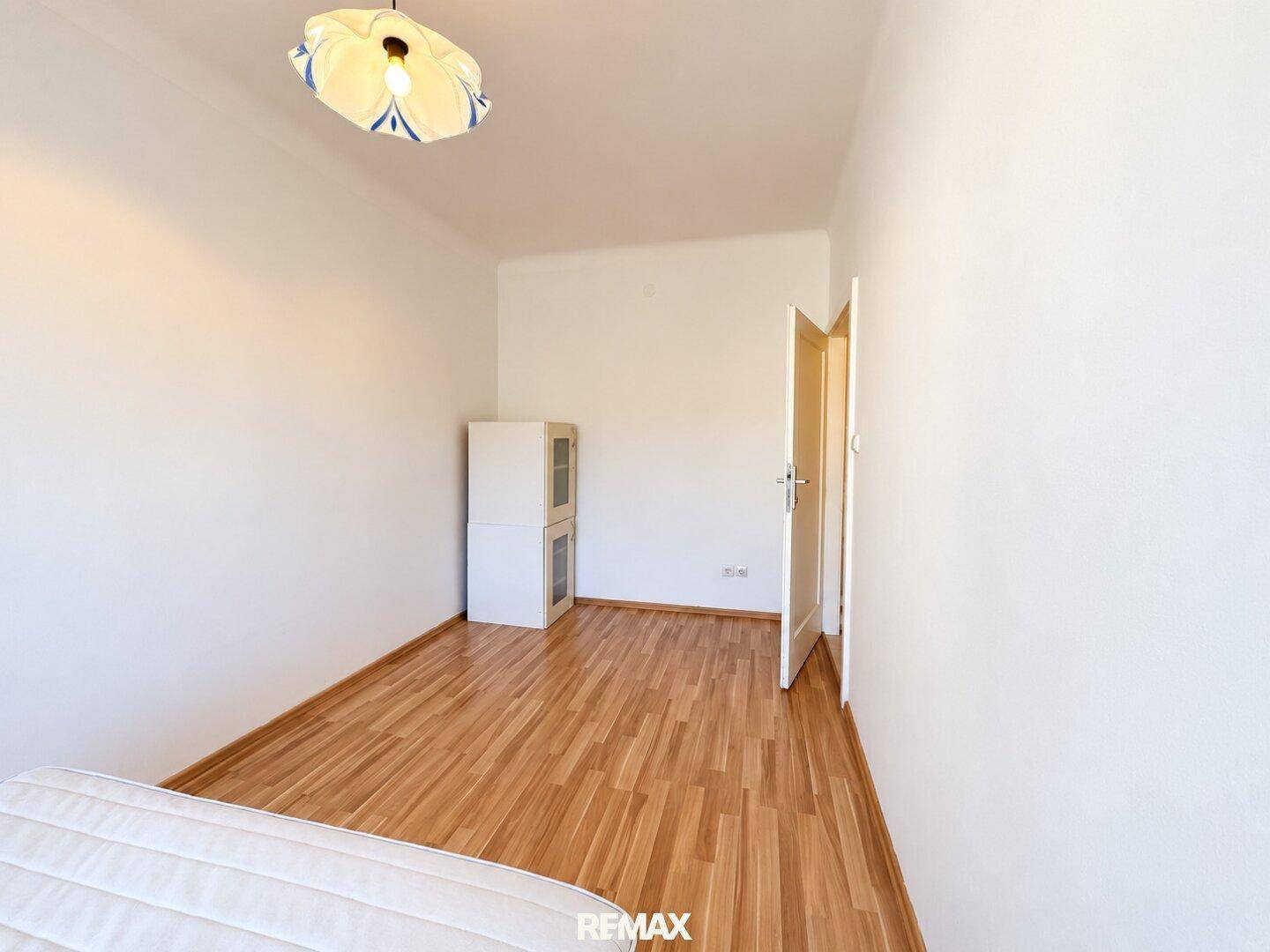 Schlafzimmer mit Holzboden und einem kleinen Schrank, mit Zugang zu einem weiteren Raum.