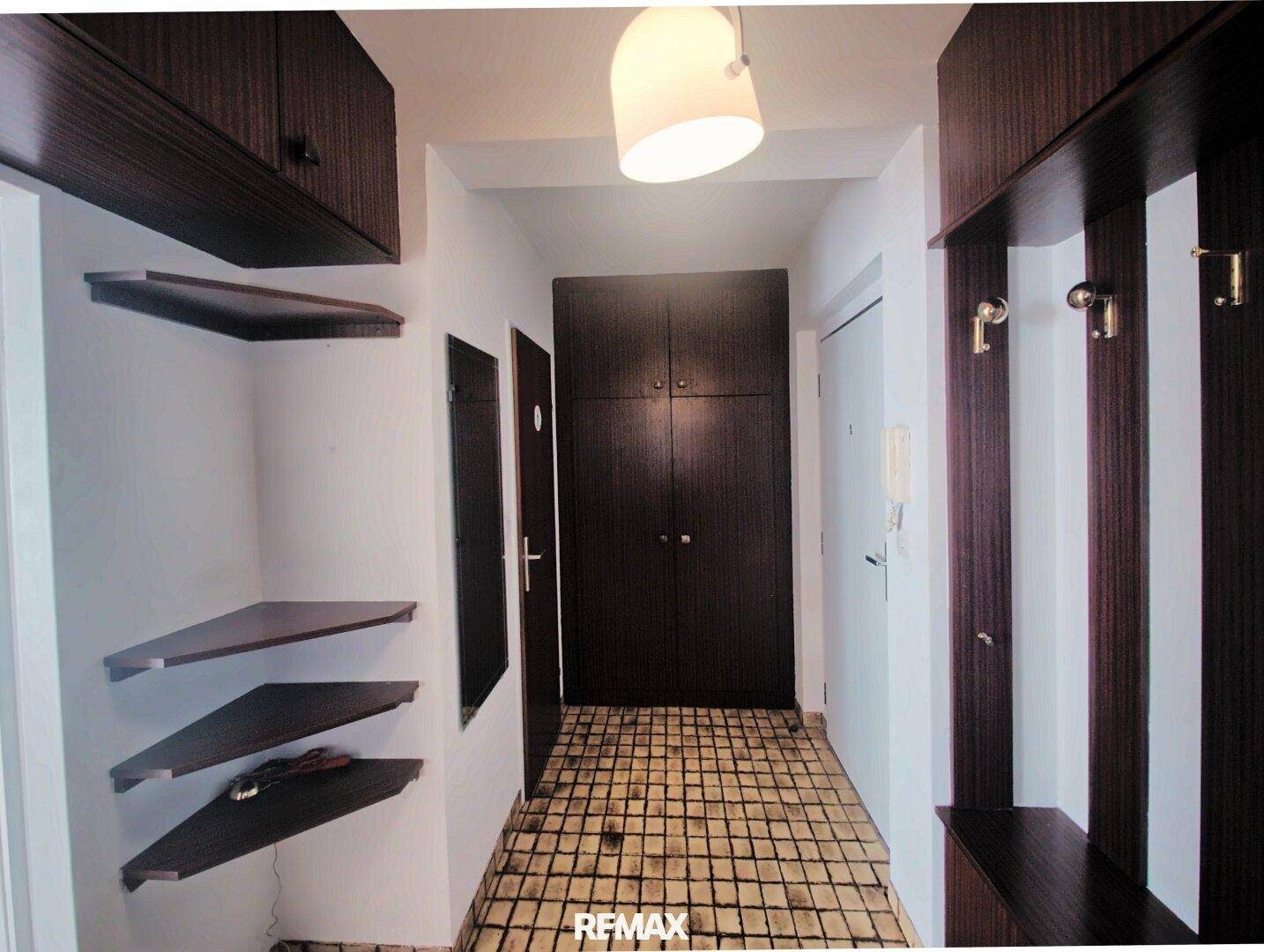 Eingangsbereich mit dunklen Holzmöbeln und einem gefliesten Boden, bietet Stauraum und Garderobe.