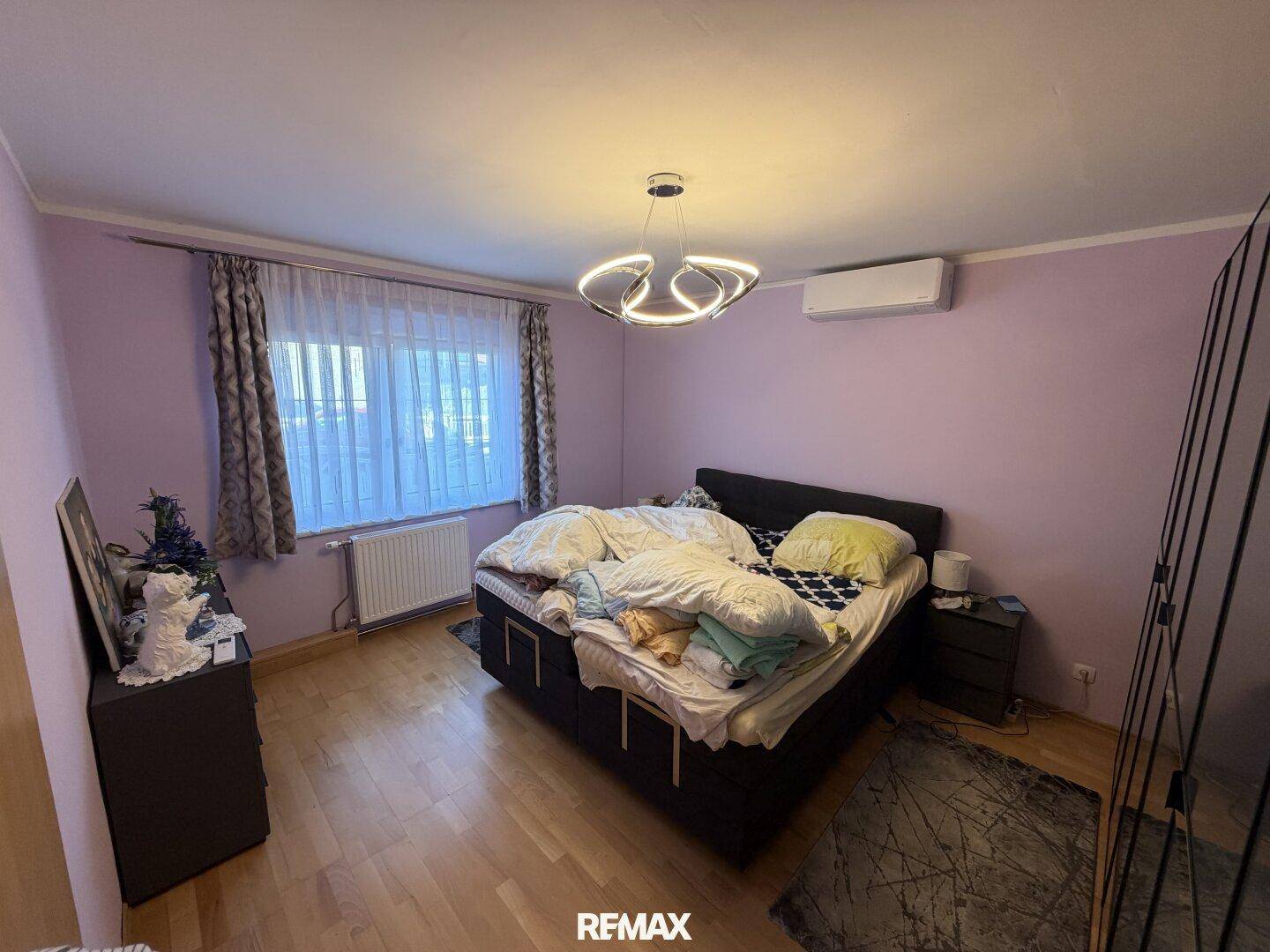 Schlafzimmer mit Doppelbett, Klimaanlage und lila Wänden, ausgestattet mit Holzboden.