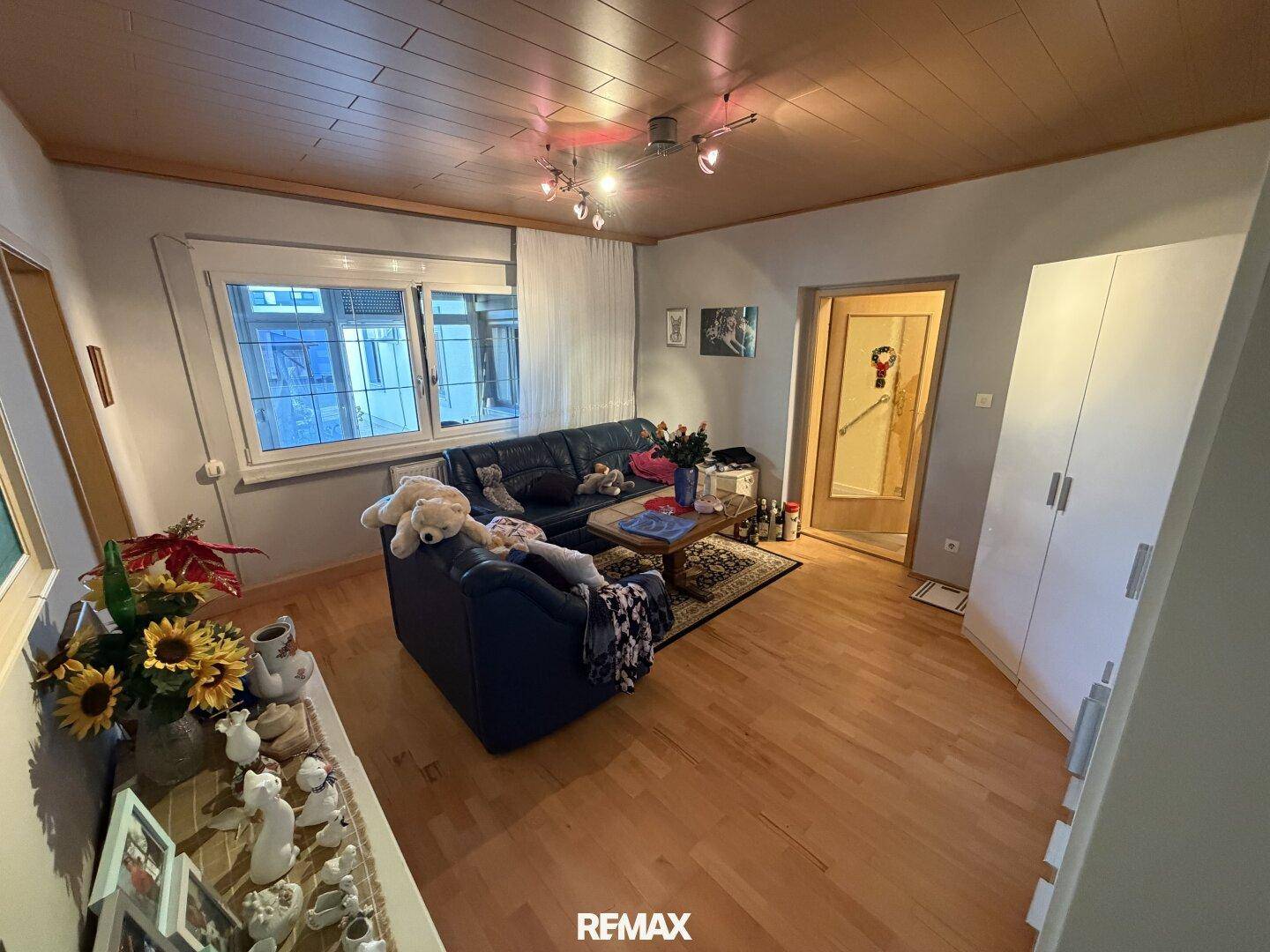 Wohnzimmer mit dunklem Ledersofa, Holzboden und Holzdeckenverkleidung.