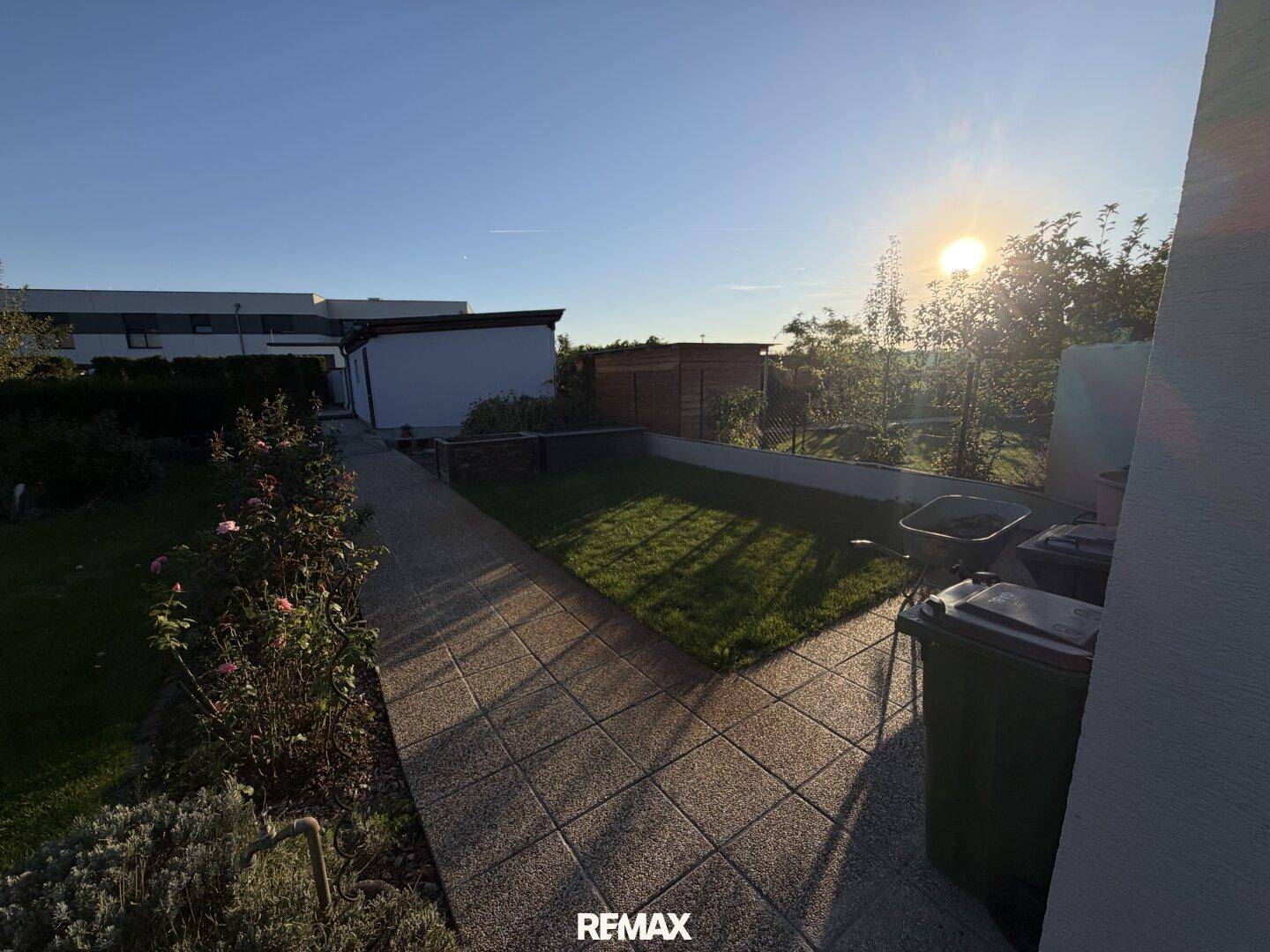 Gartenweg mit Rasenfläche und Blick in die Ferne bei Sonnenuntergang.
