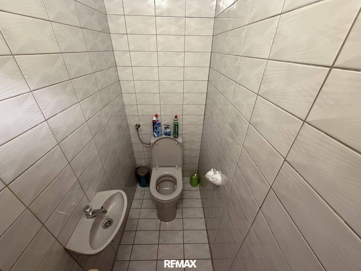 Kleines Gäste-WC mit weißen Fliesen an Wänden und Boden, inklusive Waschbecken.