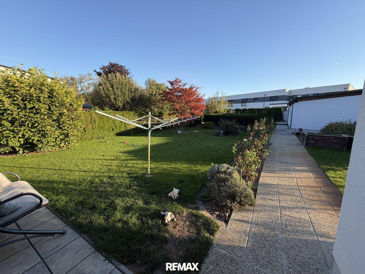 Sonniger Garten mit Wäschespinne und gepflegter Rasenfläche, umgeben von Hecken.