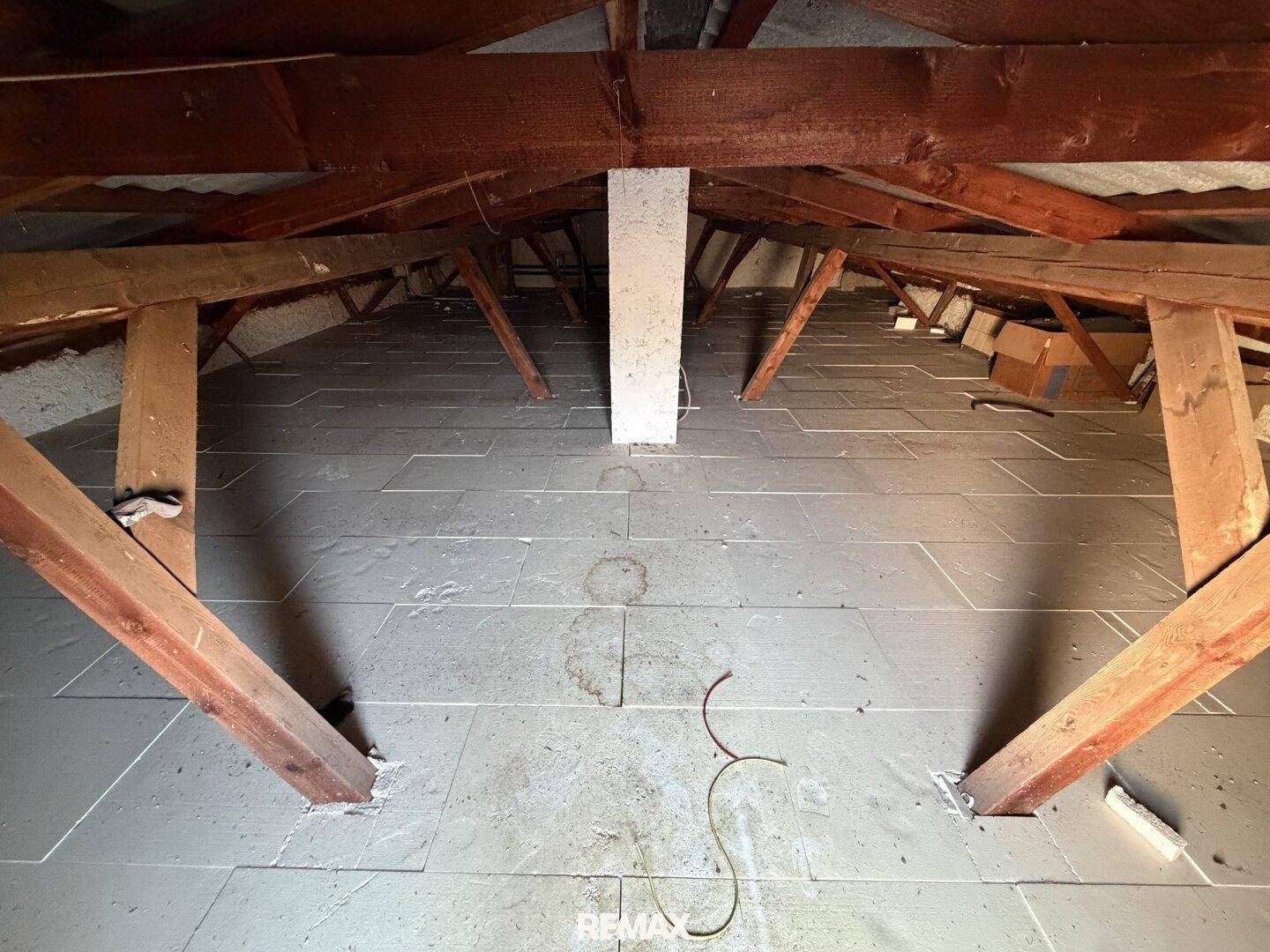 Unausgebauter Dachboden mit sichtbaren Holzbalken und Isolierung.