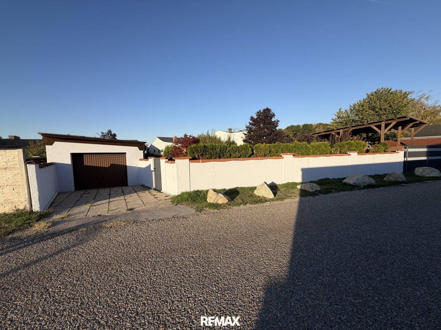Rückseite des Grundstücks mit Garage, umgeben von einer weißen Mauer und Hecken.