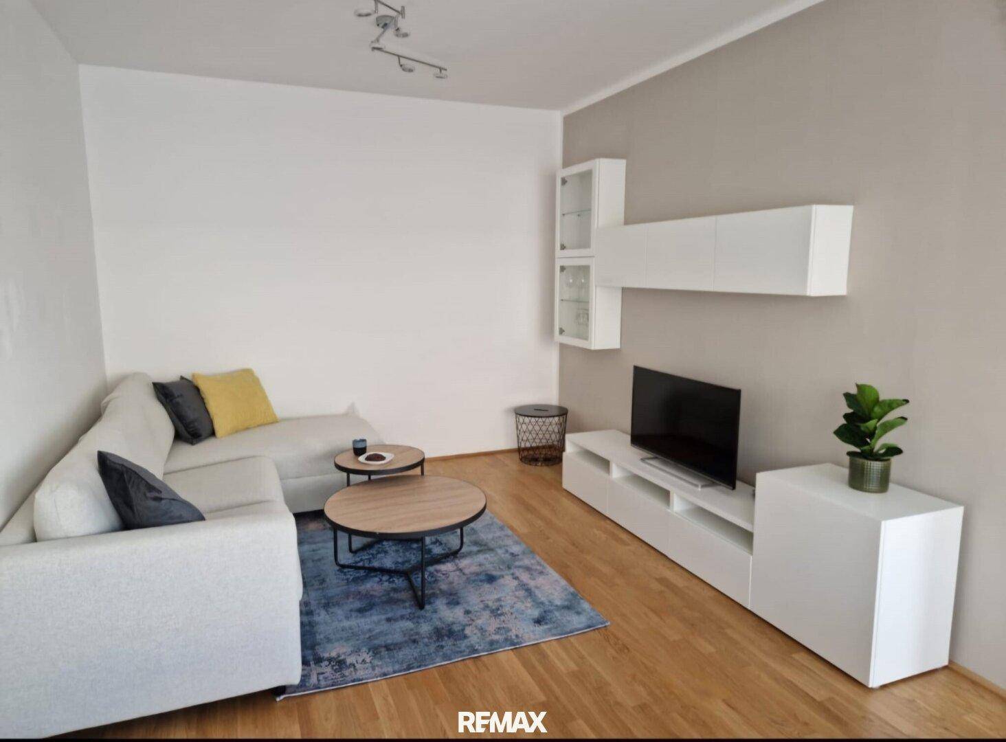 Gemütliches Wohnzimmer mit weißem Ecksofa, modernem TV-Möbel und Holzboden.