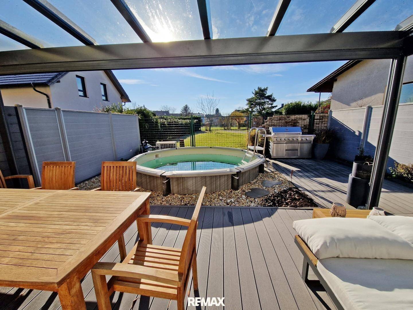 Sonniger Terrassenbereich mit Esstisch, Whirlpool und Grillstation, umgeben von einem gepflegten Garten.