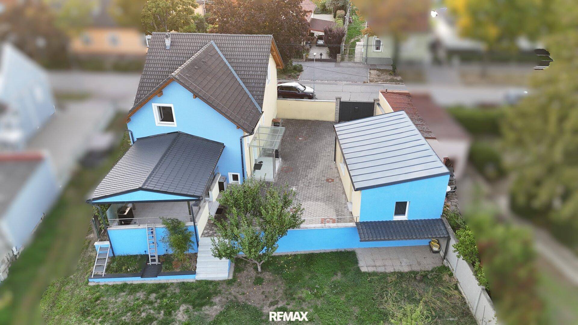 Luftaufnahme des Anwesens mit blau gestrichenem Haus, Garage und Carport in einer ruhigen Wohngegend.