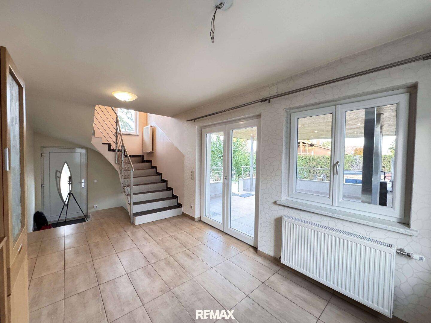 Heller Eingangsbereich mit gefliestem Boden, Treppe zum Obergeschoss und Zugang zur Terrasse.
