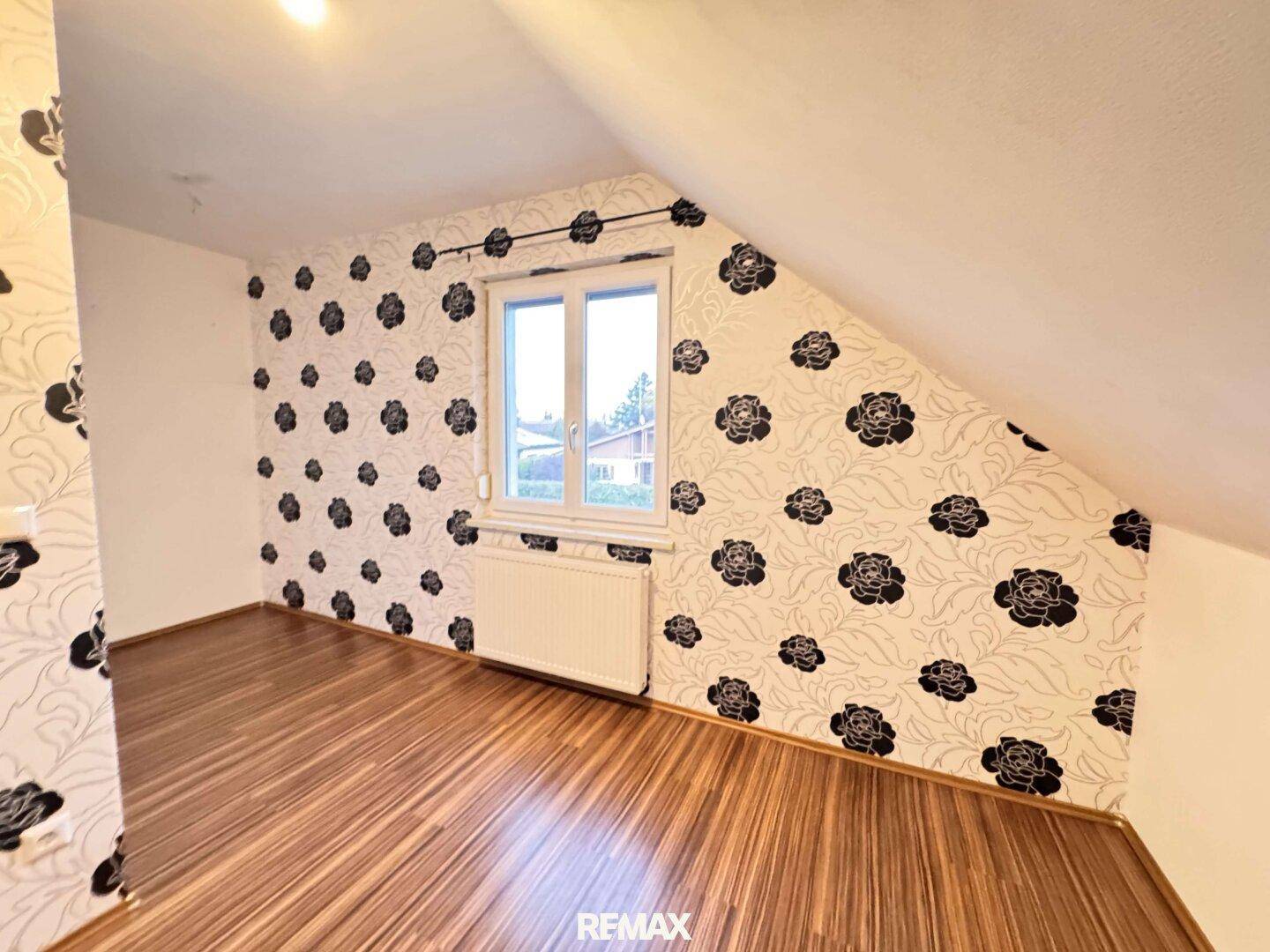 Schlafzimmer im Dachgeschoss mit floraler Tapete, Holzboden und schräger Decke.