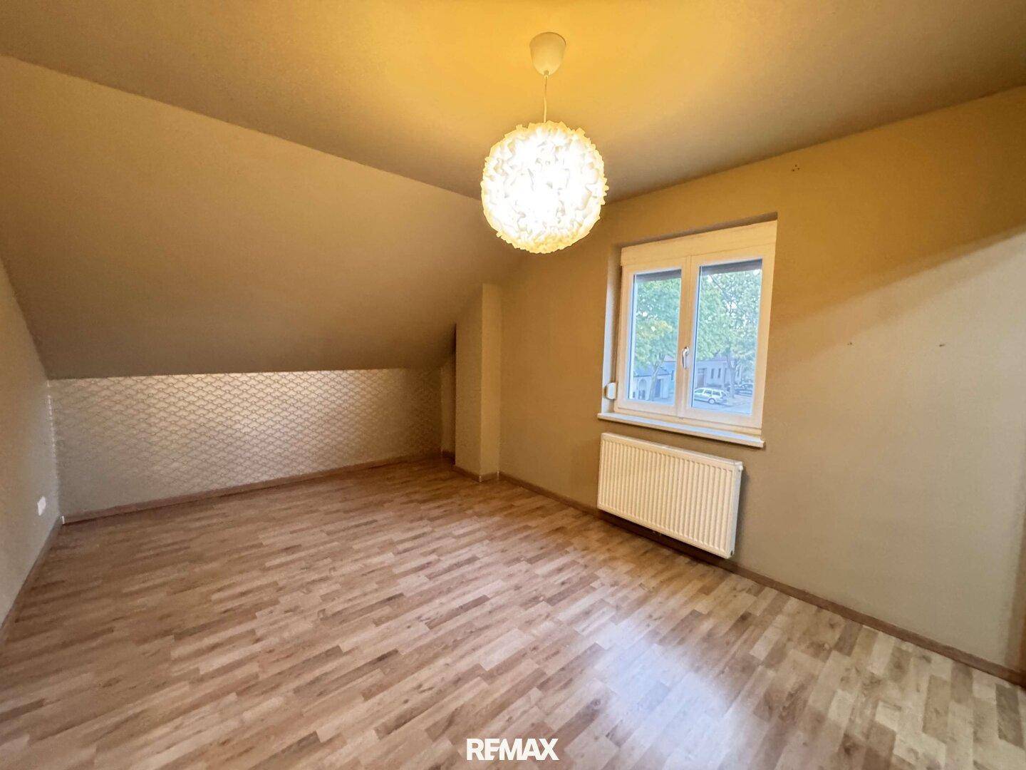 Helles Schlafzimmer im Dachgeschoss mit Holzboden, schräger Decke und Fenster.