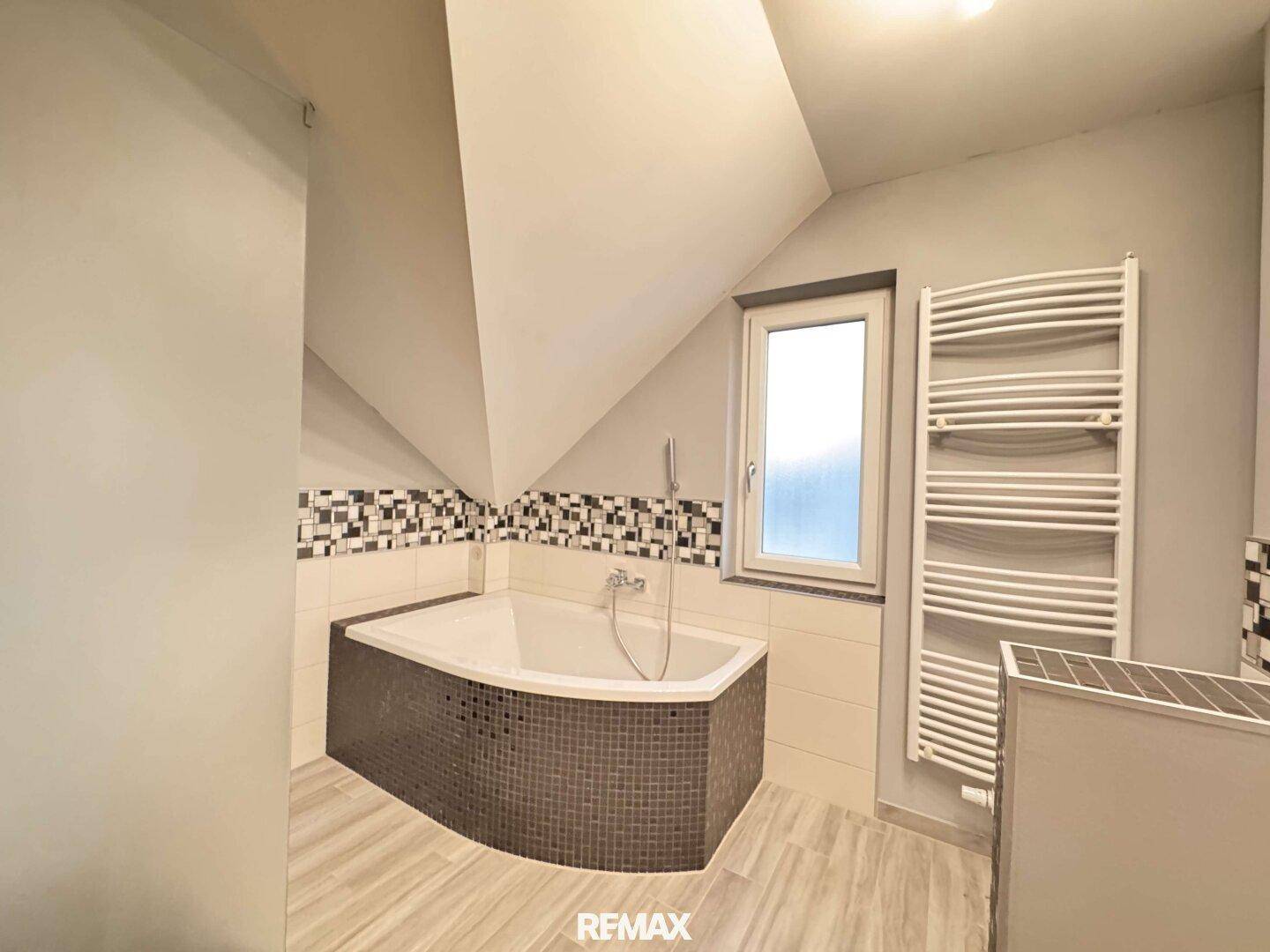 Modernes Badezimmer im Dachgeschoss mit Eckbadewanne, Fliesen und beheiztem Handtuchhalter.