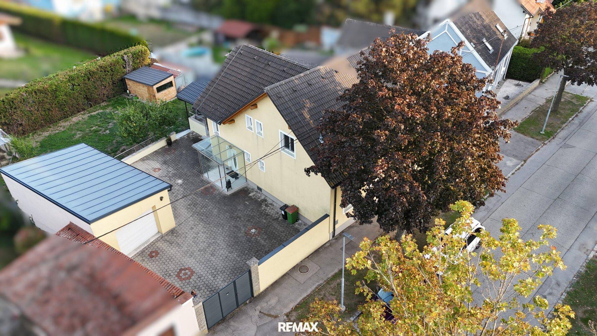 Luftaufnahme eines Einfamilienhauses mit gepflastertem Hof, Garage und umliegenden Gärten in einer Wohngegend.