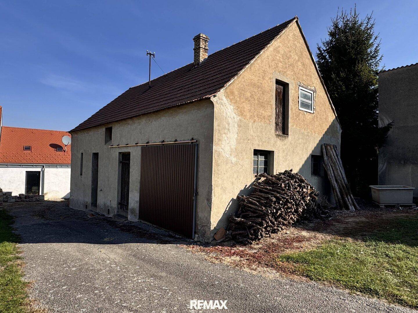 Seitenansicht des rustikalen Hauses mit Holzstapel und Garagentor.