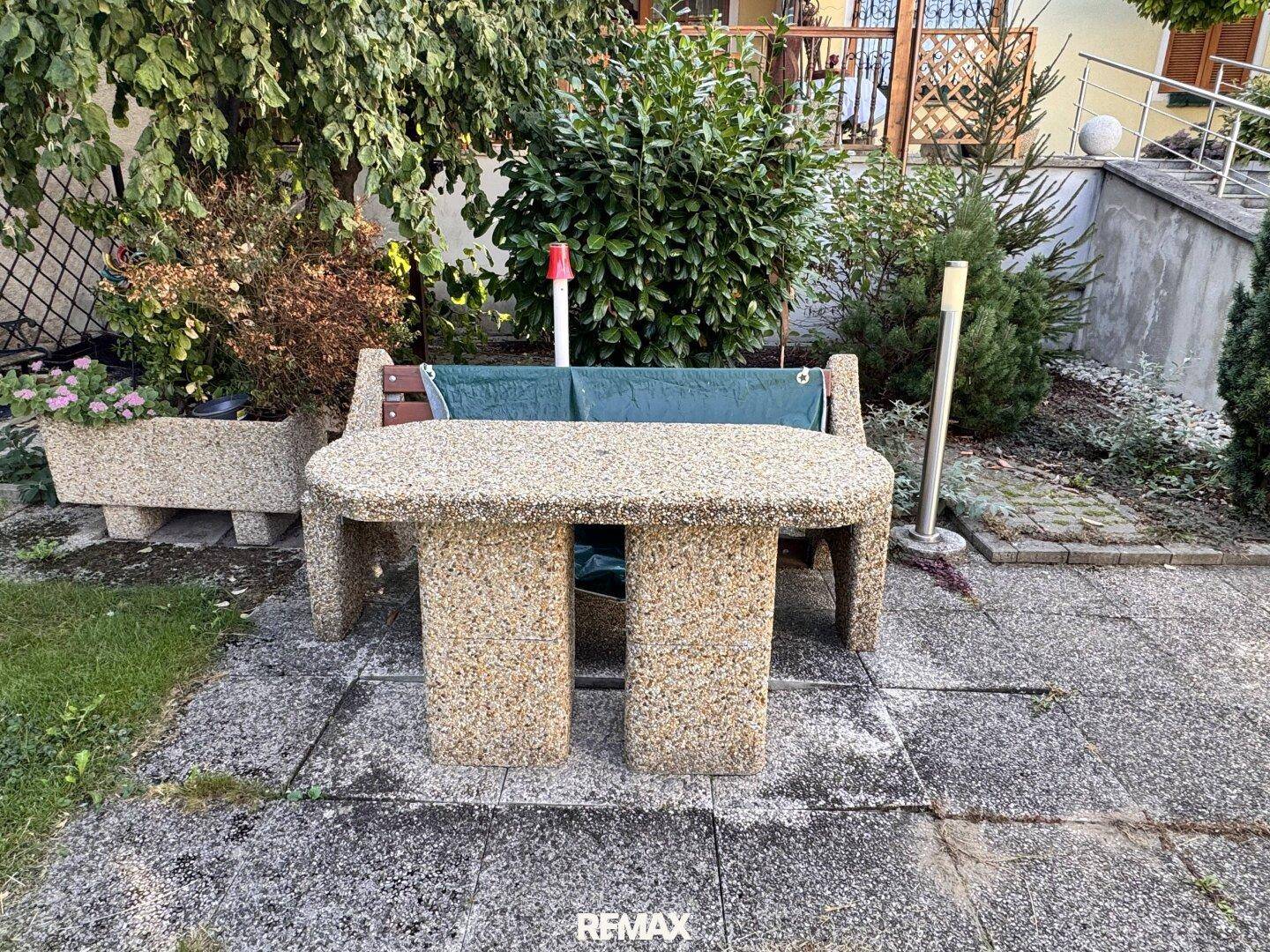 Gemütlicher Sitzbereich im Garten mit Steintisch und Bank.