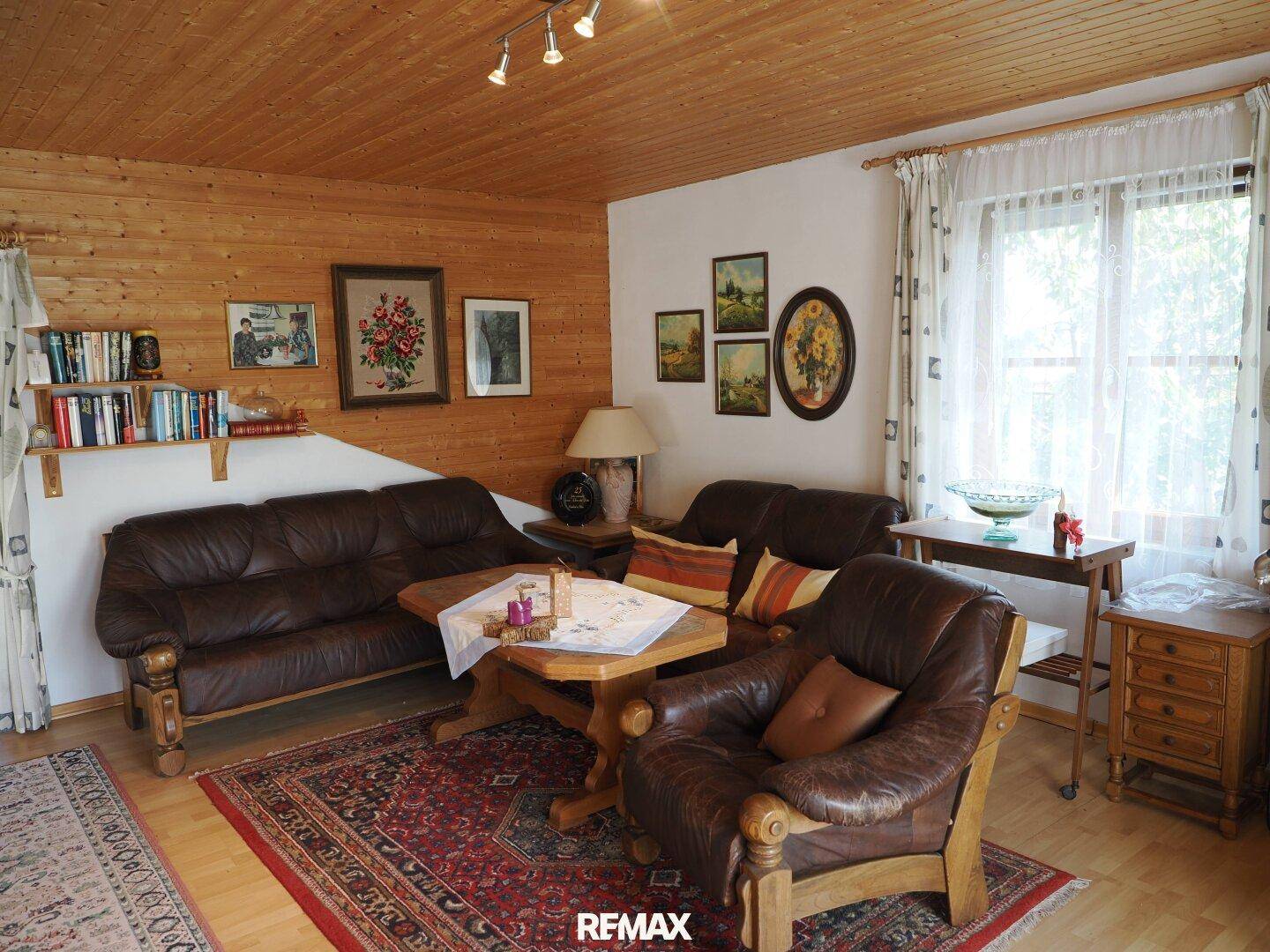 Rustikales Wohnzimmer mit Holzvertäfelung, Holzbalkendecke und bequemen Ledersofas.