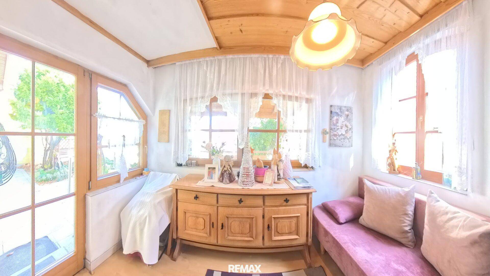 Heller Wohnraum mit Holzbalkendecke, großen Fenstern und gemütlichem Sofa.