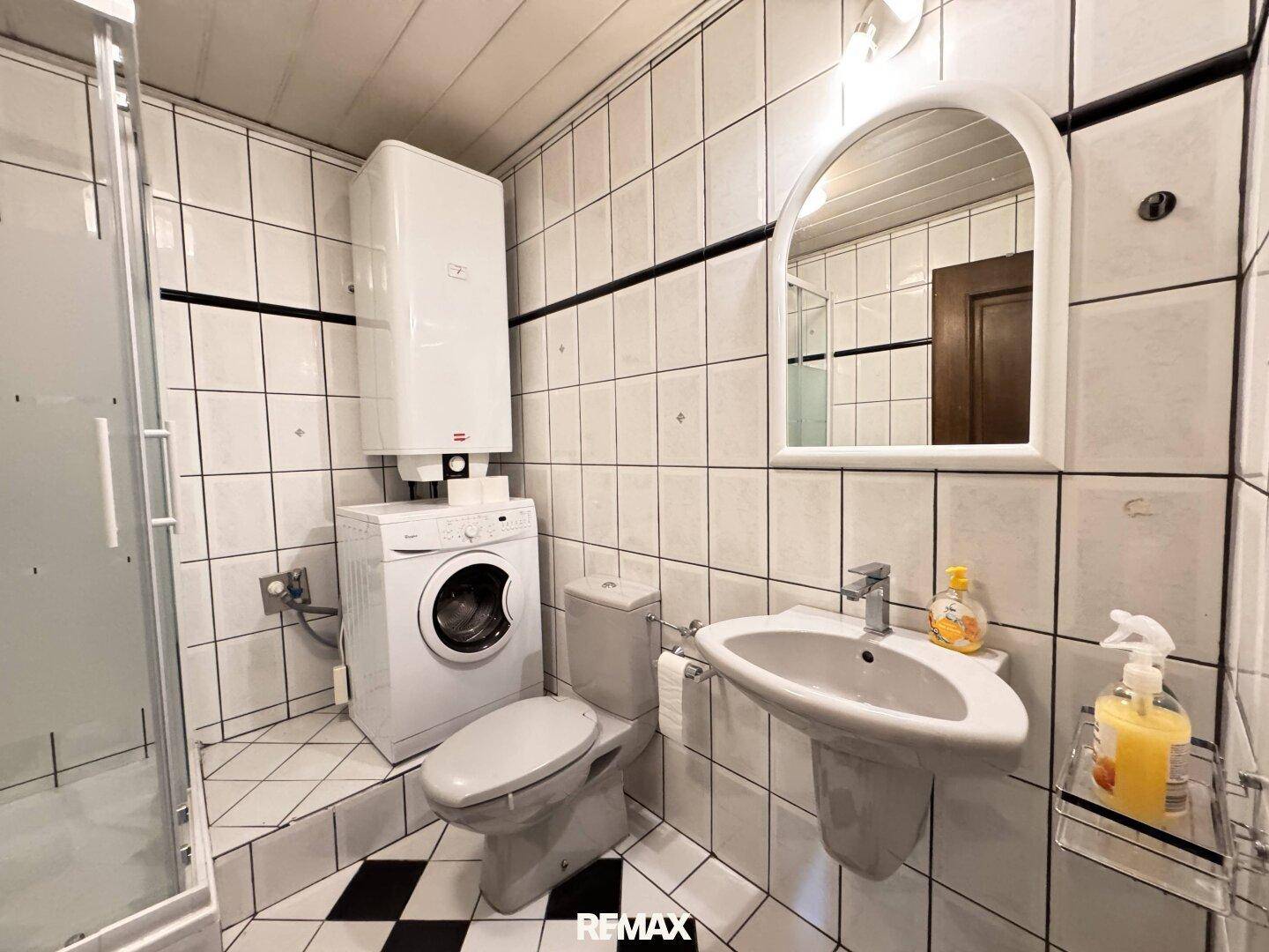Funktionales Badezimmer mit Dusche, WC, Waschbecken und Waschmaschine.