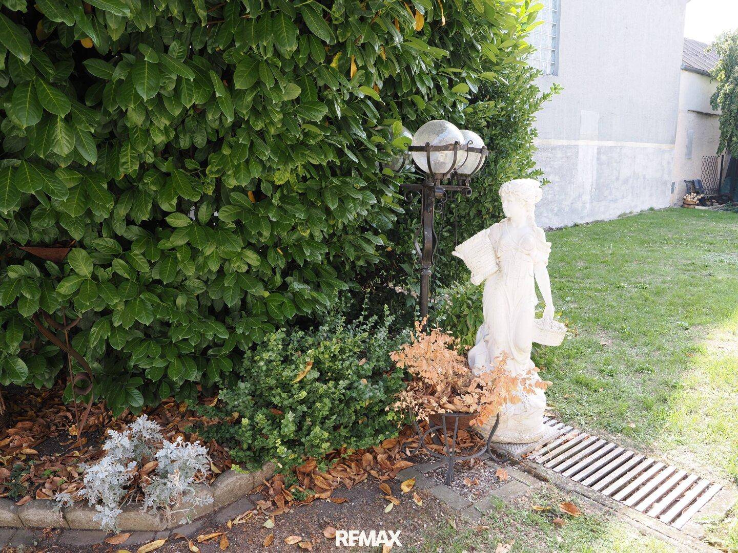 Detailansicht eines Gartens mit einer klassischen Statue und üppiger Bepflanzung.