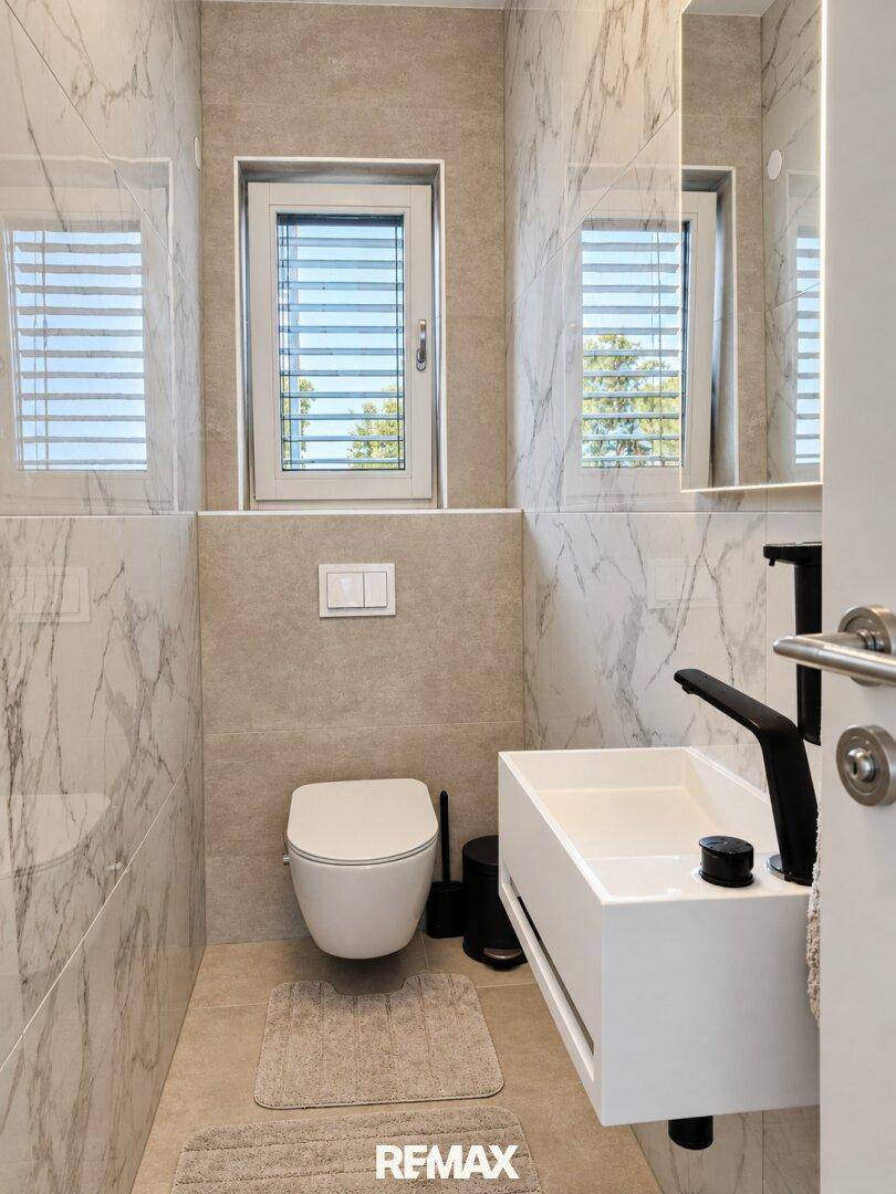 Modernes Gäste-WC mit Marmorfliesen, wandhängendem WC und kleinem Waschbecken.