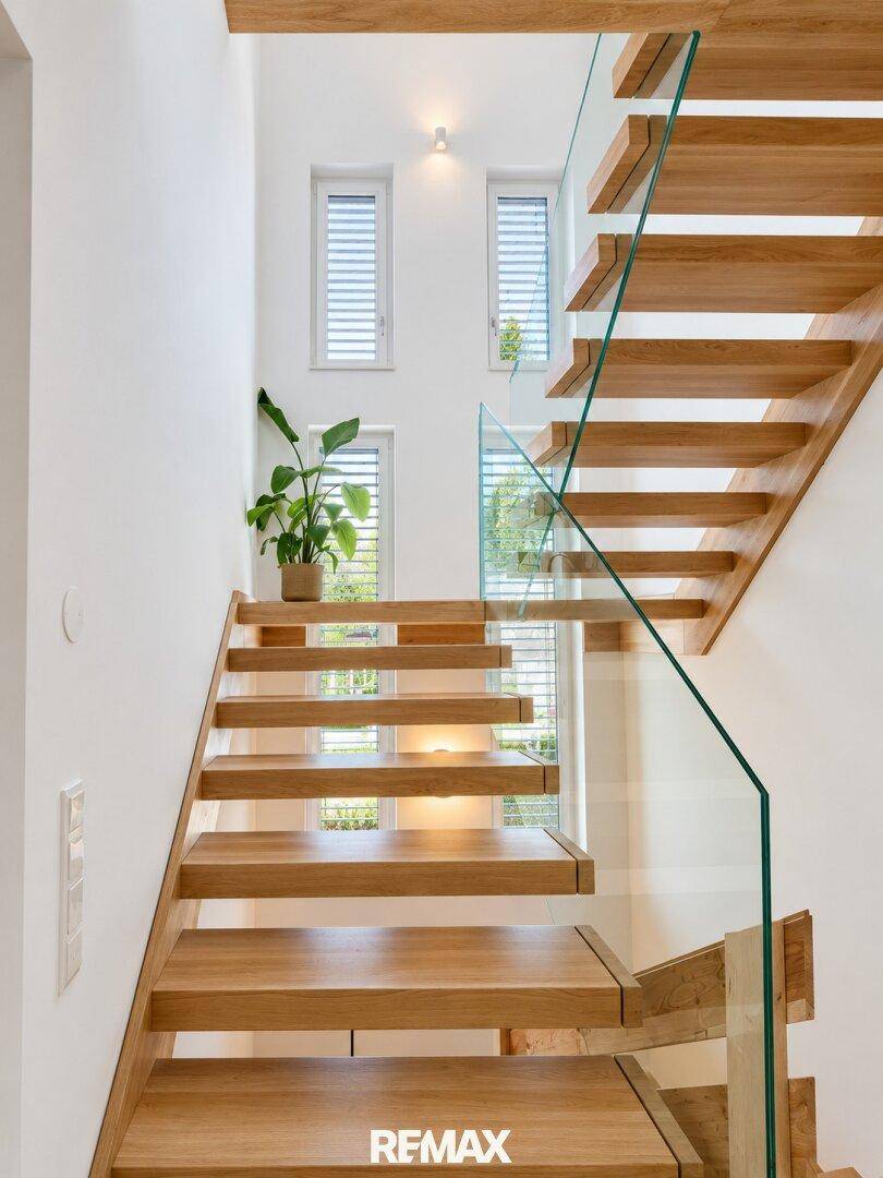 Moderne Holztreppe mit Glasgeländer und natürlichem Lichteinfall.