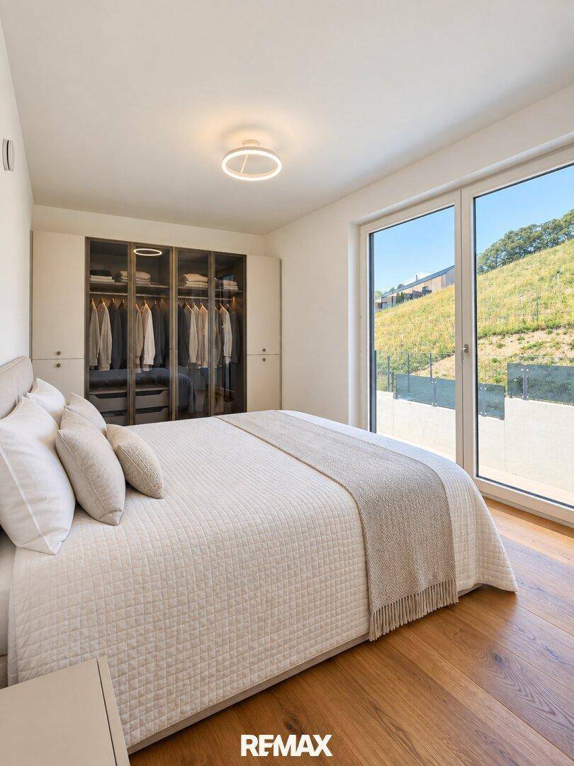 Helles Schlafzimmer mit Holzboden, Einbauschrank und großem Fenster mit Blick ins Grüne.