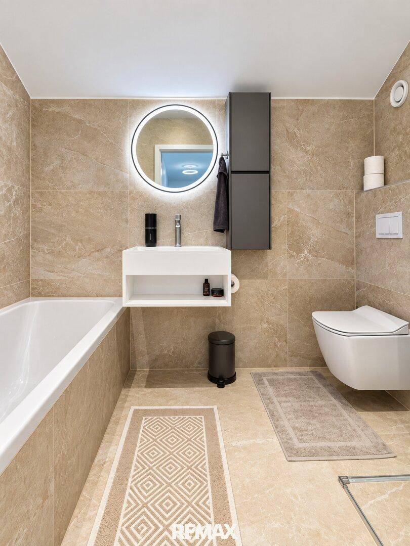 Modernes Badezimmer mit Badewanne, wandhängendem WC und beleuchtetem Spiegel.