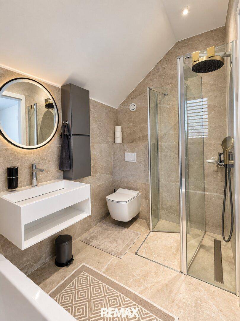 Modernes Badezimmer mit begehbarer Dusche, Dachschräge und beleuchtetem Spiegel.