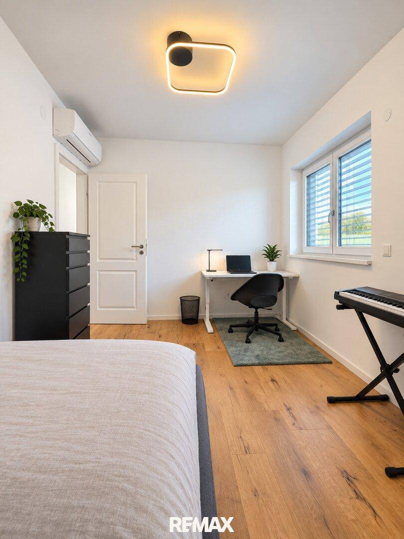Helles Schlafzimmer mit Holzboden, Schreibtisch und Klimaanlage.
