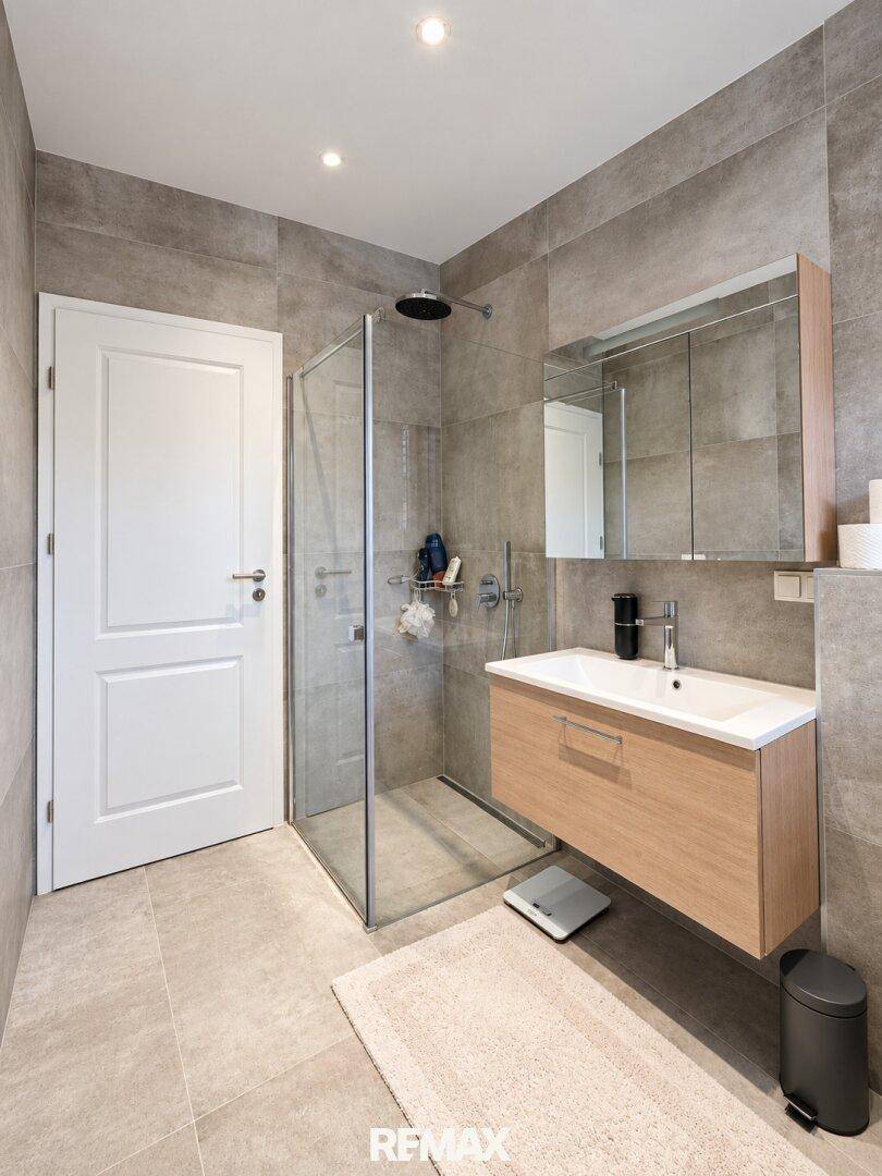 Modernes Badezimmer mit Dusche, Holzwaschtisch und großformatigen Fliesen.