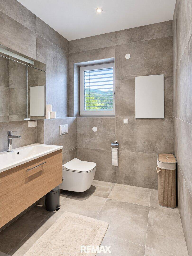 Modernes Badezimmer mit Fenster, wandhängendem WC und Holzwaschtisch.