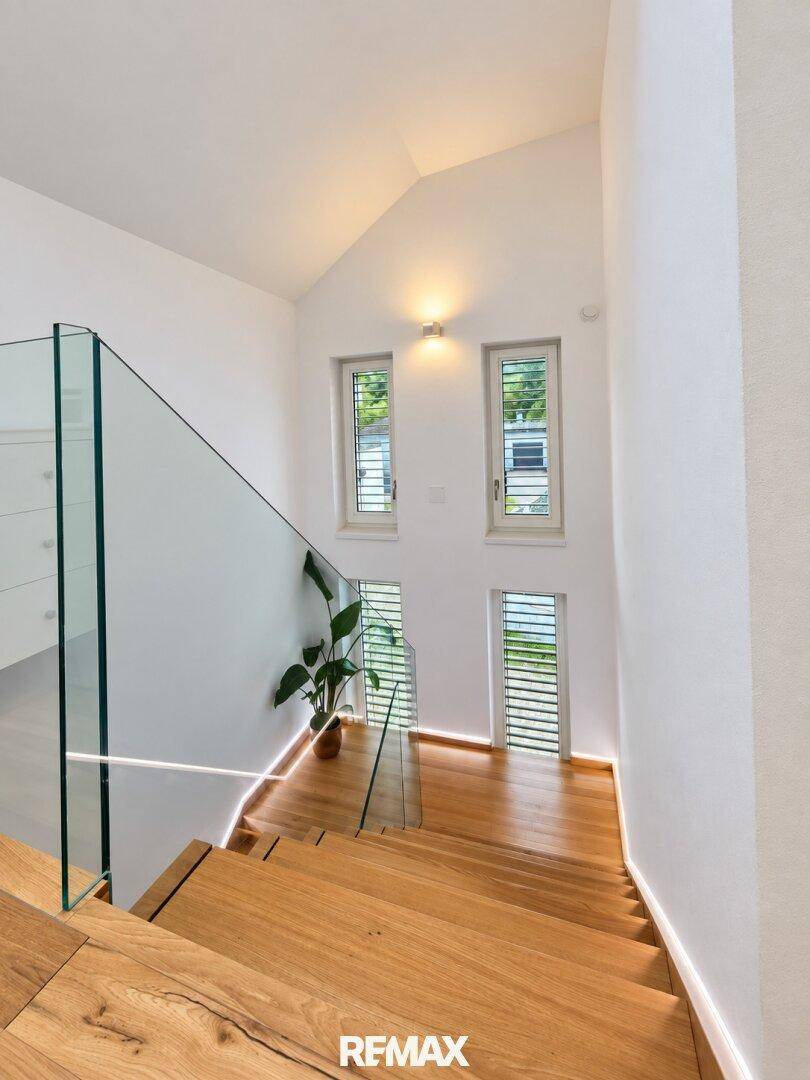 Heller Treppenaufgang mit Holzstufen, Glasgeländer und indirekter Beleuchtung.