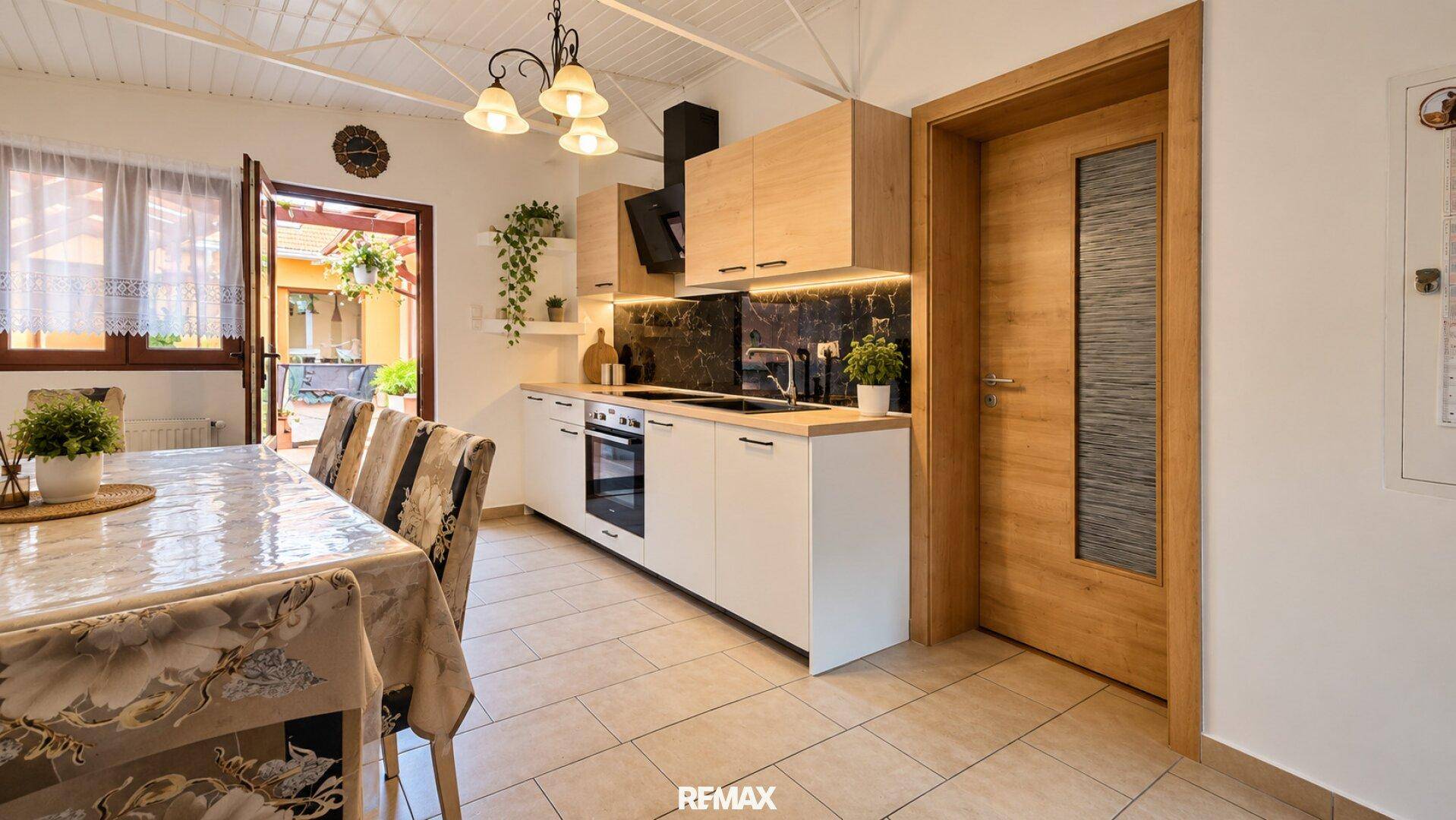 Moderne Küche mit hellen Holz- und weißen Fronten, Essbereich und Zugang zum Außenbereich.