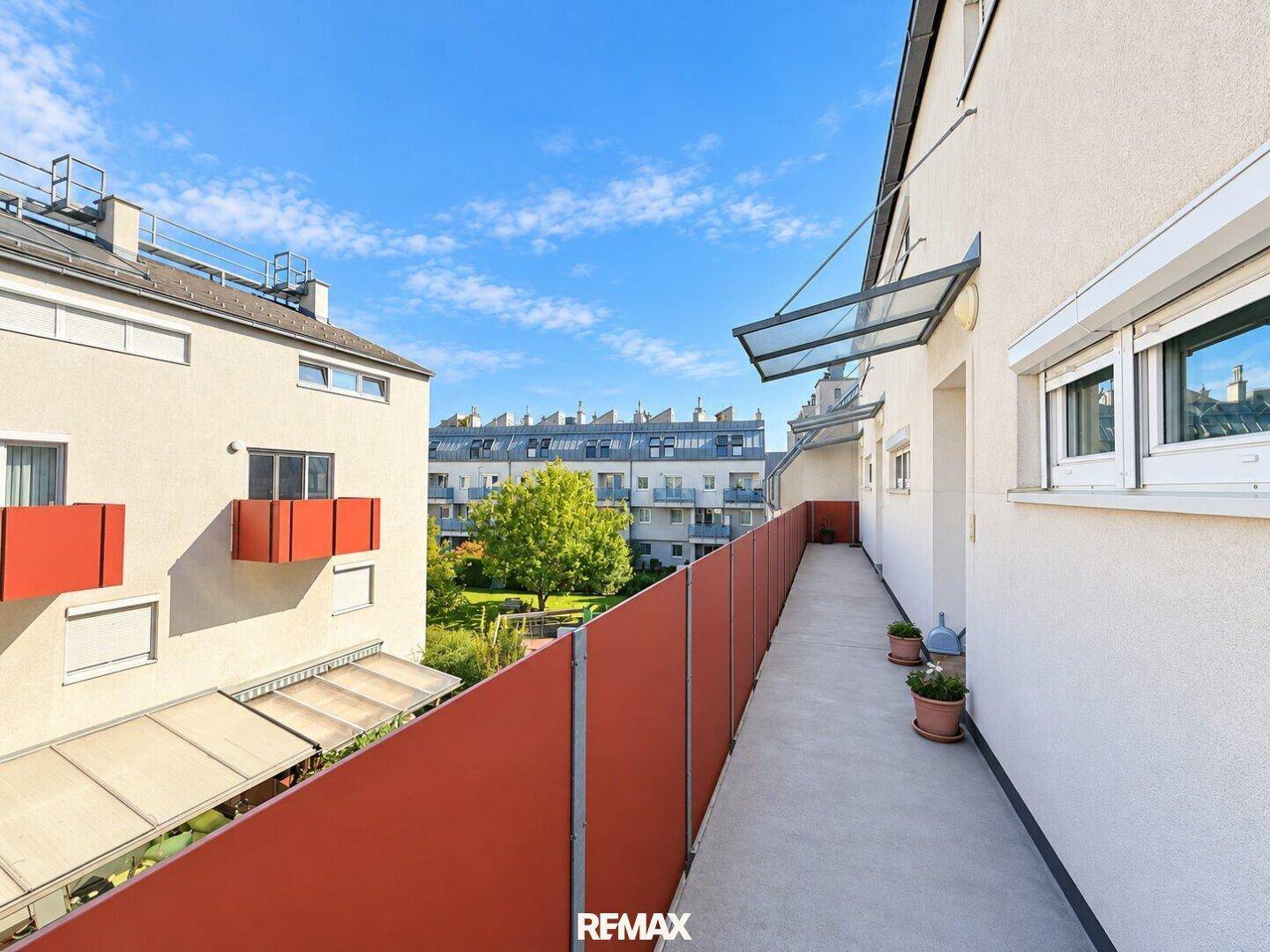 Langer Balkon mit rotem Sichtschutz und Blick auf den Innenhof.