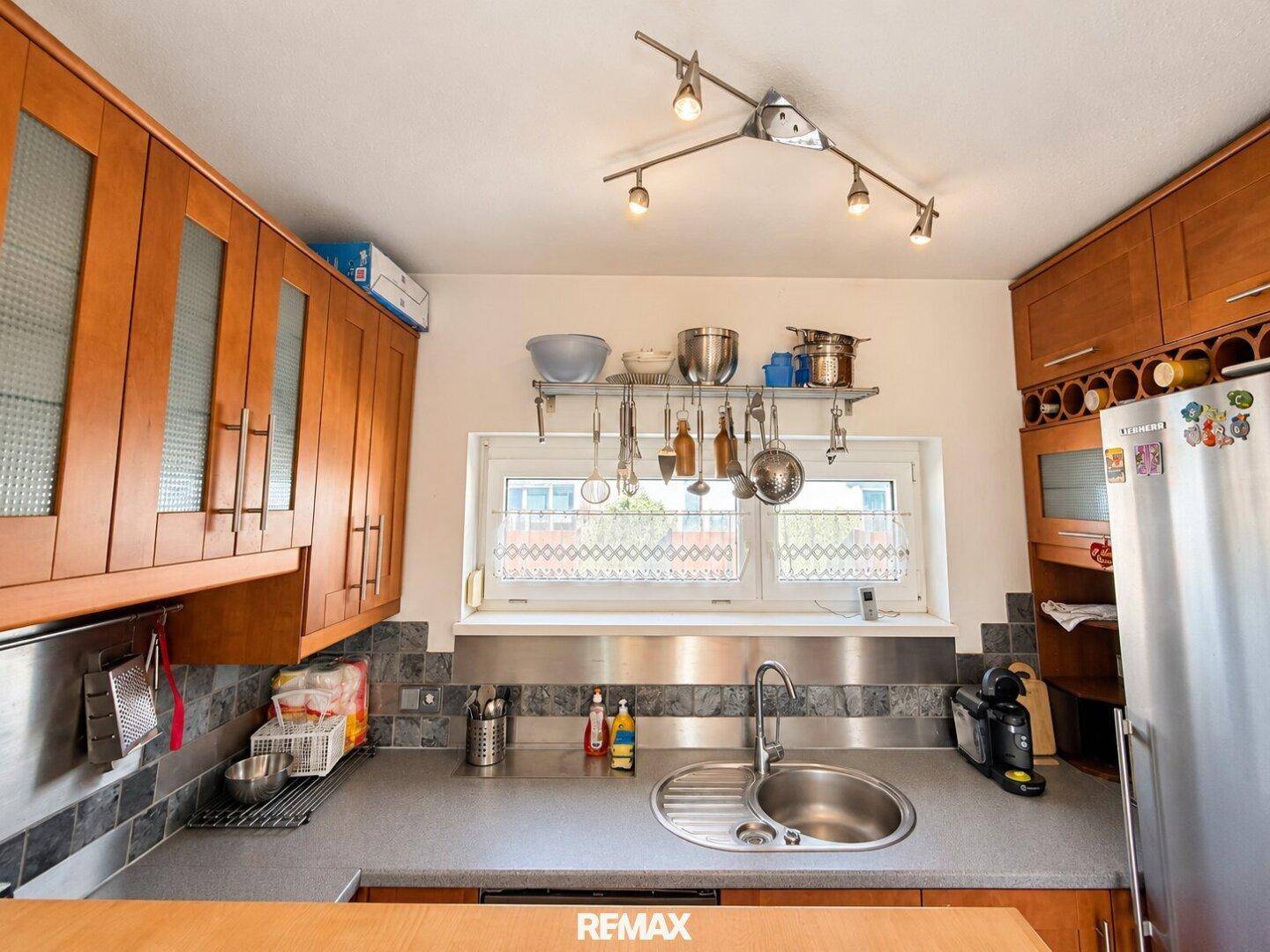 Helle Küche mit Fenster, Spüle, Kühlschrank und Holzschränken.