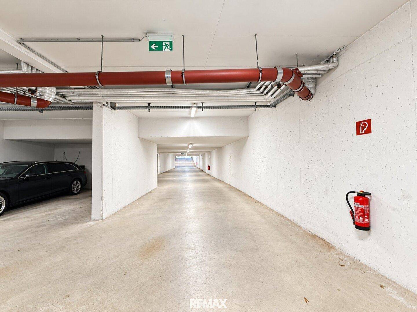 Lange Tiefgarage mit Betonboden und sichtbaren Leitungen an der Decke.